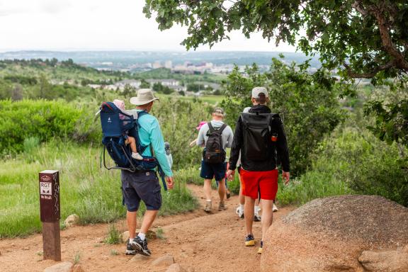 People in outdoor equipment wearing backpacks hike on a trail in Colorado Springs.
