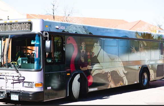 A Mountain Metro Transit bus with an art wrap featuring a dog jumping on a human. The art was designed by Palmer High School students.