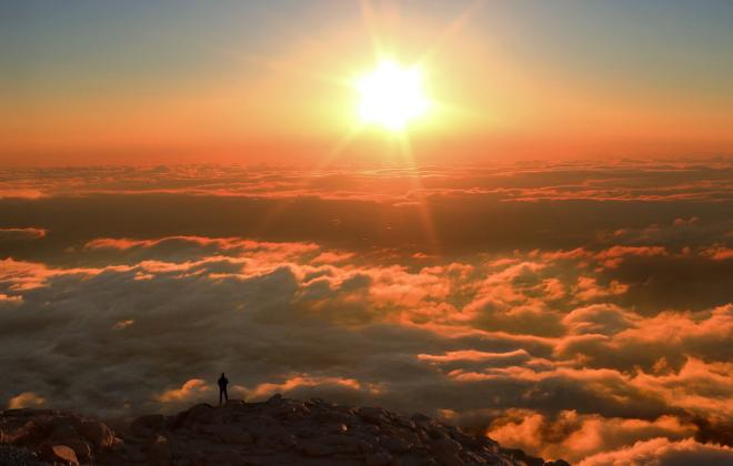 Silhouette of a man standing atop a rocky area on the summit of Pikes Peak at sunrise.